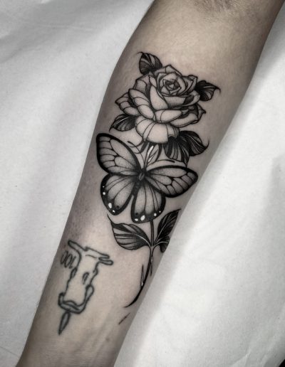 Tatuaje blackwork en Barcelona con diseño de rosa y mariposa en el antebrazo. Sombras detalladas y líneas nítidas en Black Haru Tattoo Studio.