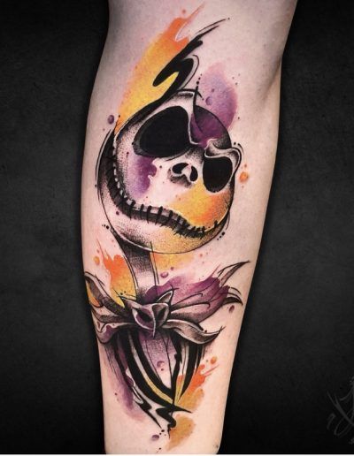 Tatuaje a color de Jack Skellington en estilo acuarela, con tonos naranjas, morados y negros difuminados, creando un efecto artístico dinámico. La pieza resalta por su trazo expresivo y su fusión de colores vibrantes.
