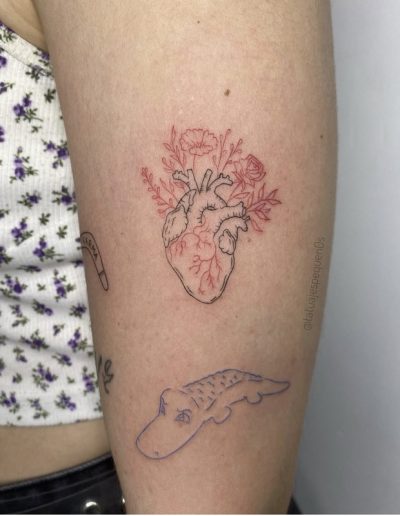 Tatuaje de estilo fineline en Barcelona con diseño de un corazón anatómico con flores en tinta negra y roja. Realizado en Black Haru Tattoo Studio.